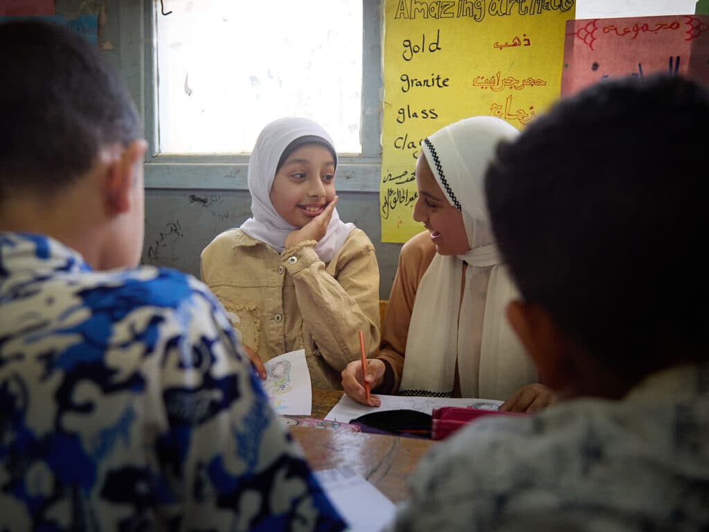 Foto: Sima Diab Två flickor i vit hijab sitter i en skolbänk och pratar med varandra.